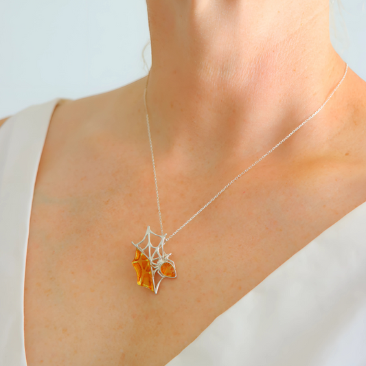 Amber Necklace with a spider web-shaped pendant featuring an orange gemstone on a plain background