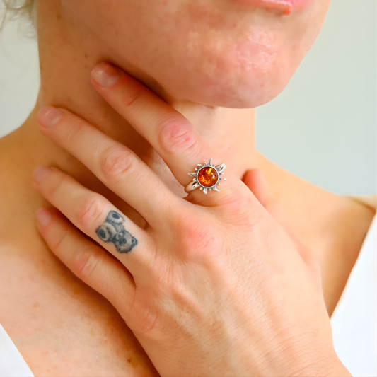 Close-up of a person wearing a silver amber ring with a sun design on their finger.