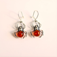Spider sterling silver earrings with amber-colored orbs on a light pink background