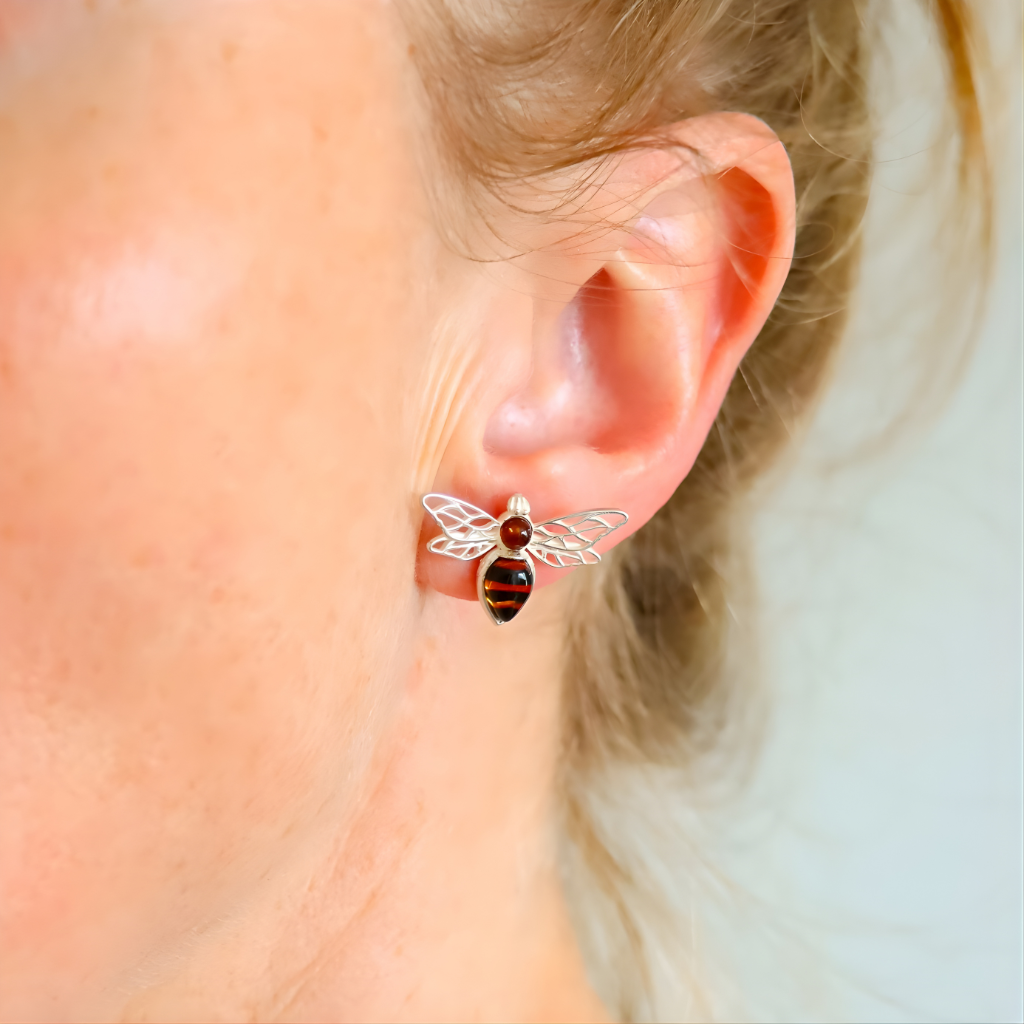 Close-up of an ear wearing a silver bee-shaped amber earring with a red and black design.