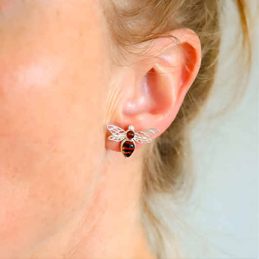 Close-up of an ear wearing a silver bee-shaped amber earring with a red and black design.