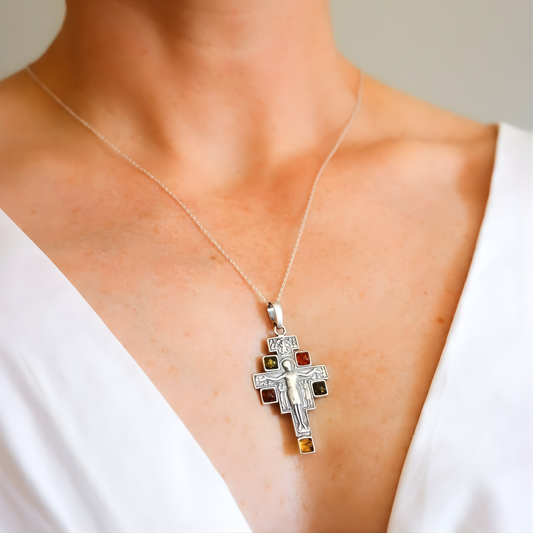 amber cross necklace with colored stones on a person wearing a white top.