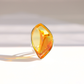 A teardrop-shaped amber gemstone statement ring with a polished silver setting, photographed on a clean white surface with soft shadows.