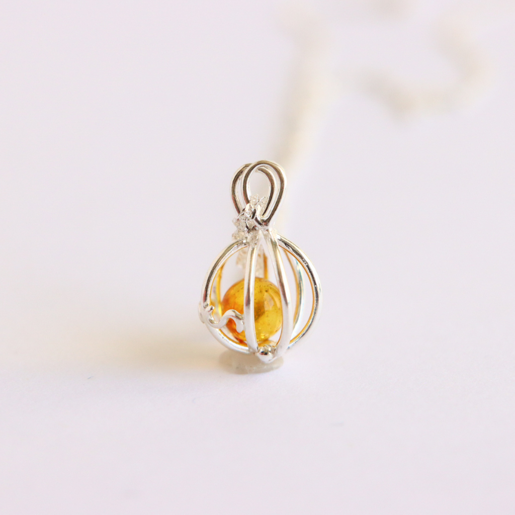 Silver cage pendant with a yellow gemstone on a light background