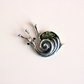 A silver amber snail pendant with a textured green shell, photographed on a solid pale pink background.