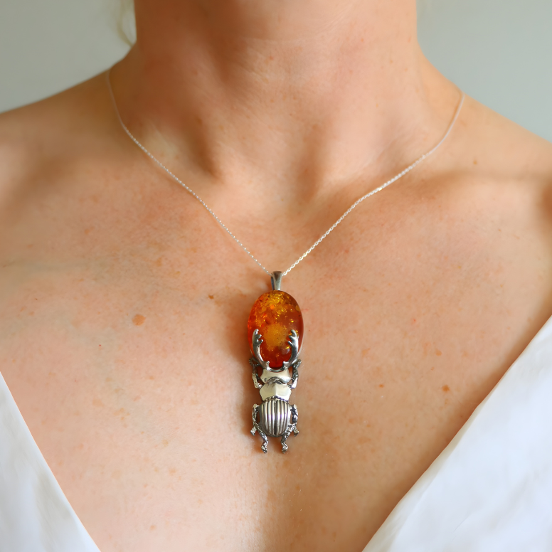 Person wearing a necklace with an amber pendant and silver beetle design.