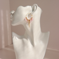 A pair of gold kunzite dagger hoop earrings with dangling lavender daggers and small gold beads, displayed on a white ceramic female bust against a soft pink background.