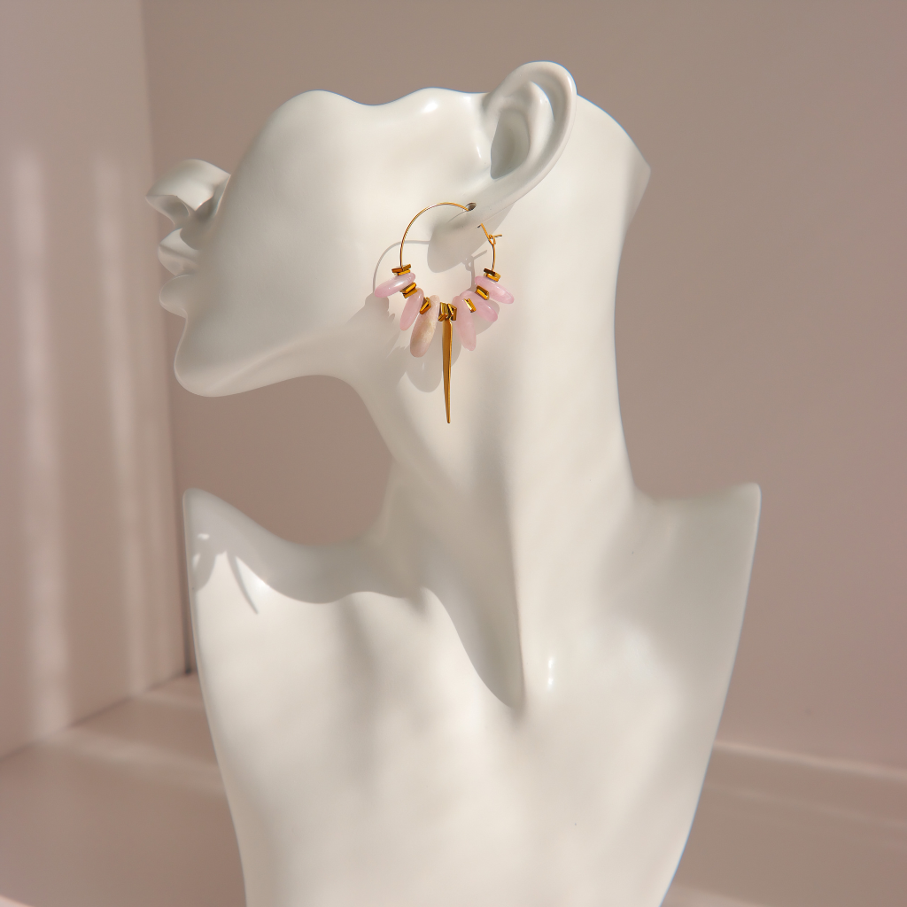 A pair of gold kunzite dagger hoop earrings with dangling lavender daggers and small gold beads, displayed on a white ceramic female bust against a soft pink background.