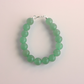 Green beaded jade bracelet on a light pink background