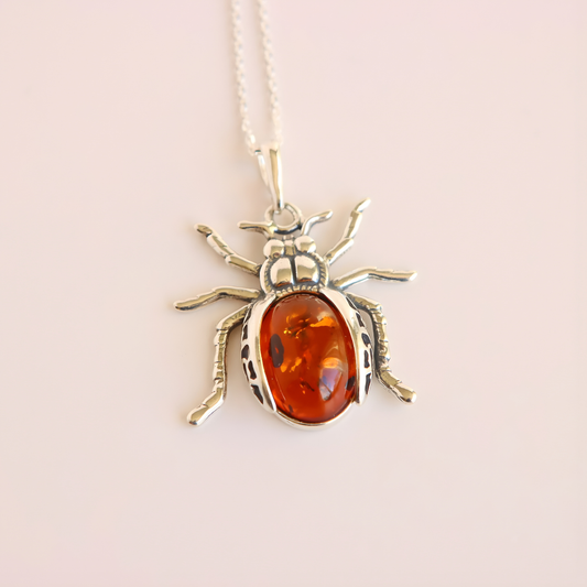 Silver amber pendant necklace with amber stone on a light pink background