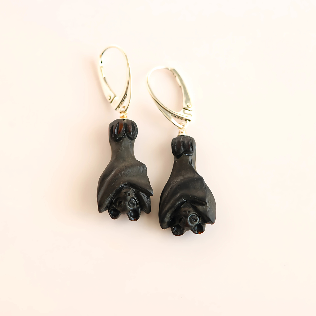 Black amber bat earrings on a light pink background