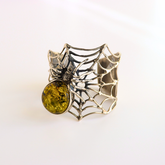 A silver spider amber bracelet  with an intricate web design and a round yellow-green stone, photographed on a clean white background.