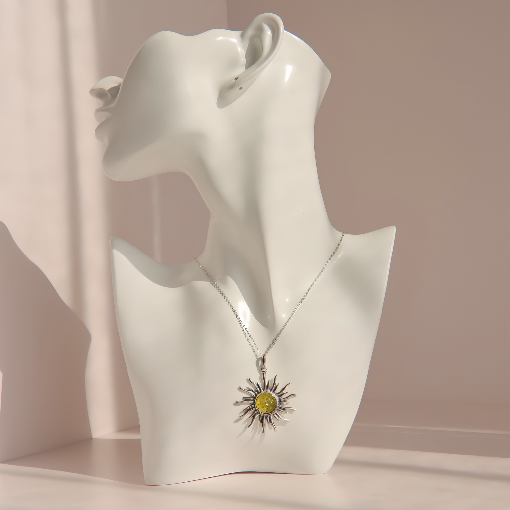 A silver lemon Baltic amber sun pendant necklace with a yellow center, displayed on a white ceramic mannequin bust against a soft beige background.