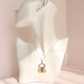 A silver spider pendant amber necklace with a central amber-orange gemstone, displayed on a white female mannequin bust against a soft pink background.