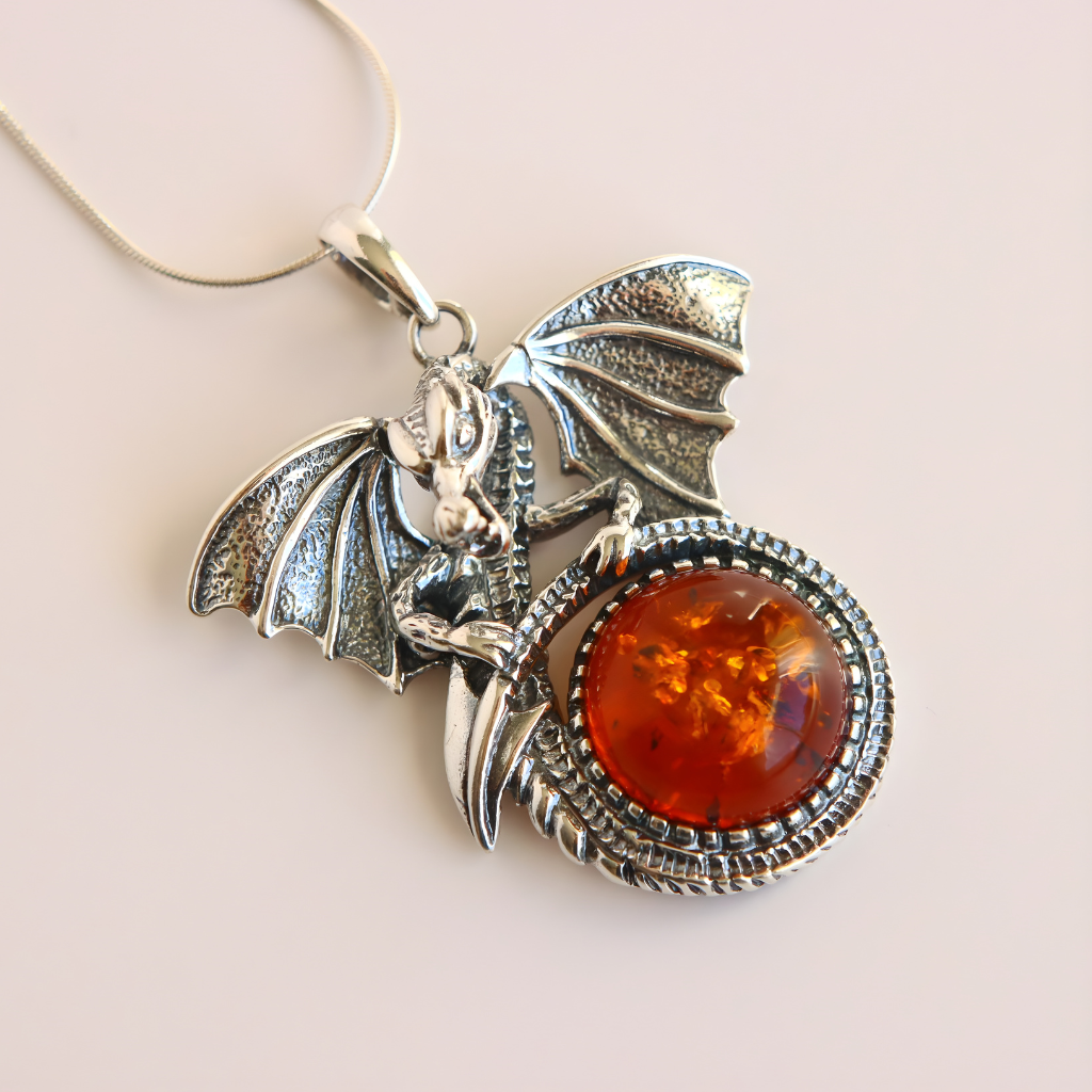 Silver dragon pendant design and amber stone on a light background