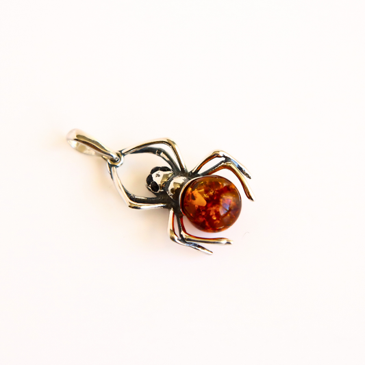 A amber spider pendant charm with a polished amber-colored round body and silver-toned legs, shown on a plain white background.