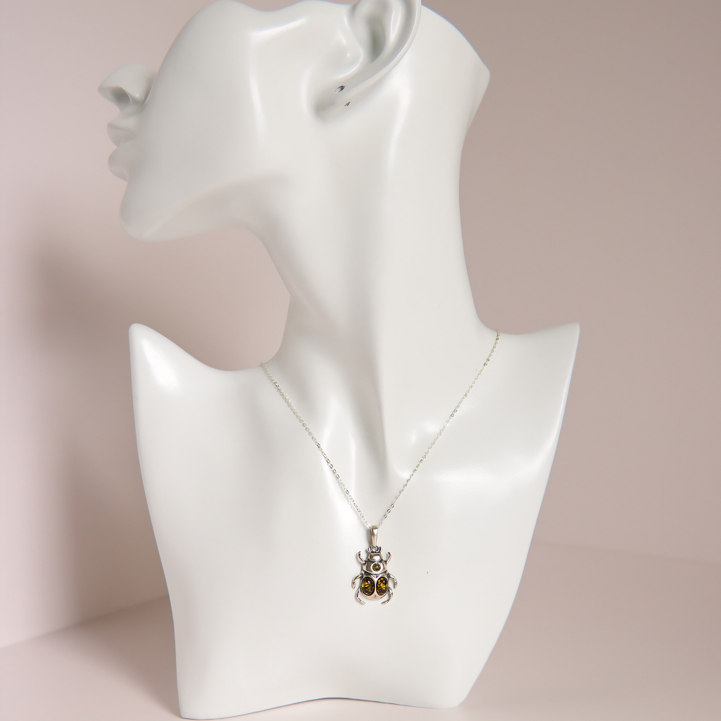 A silver pendant amber necklace with two small amber-brown stones, displayed on a white ceramic mannequin bust against a soft pink background.