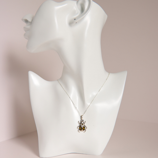 A silver pendant amber necklace with two small amber-brown stones, displayed on a white ceramic mannequin bust against a soft pink background.
