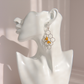 A silver-toned honeycomb dangle earring with two small yellow bee charms, displayed on a white ceramic female bust against a soft beige background.