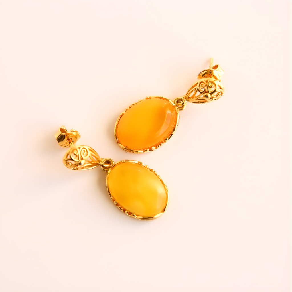 Pair of gold earrings with amber-colored stones on a light pink background