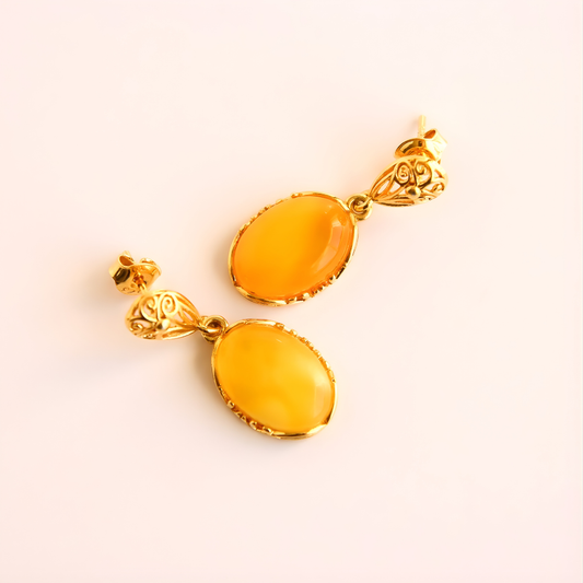 Pair of gold earrings with amber-colored stones on a light pink background