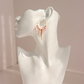 A pair of gold kunzite hoop earrings with dangling pink beads and gold charms, displayed on a white ceramic mannequin head against a soft pink background.