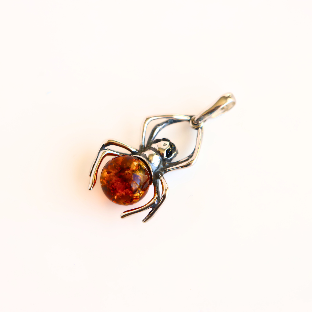 A amber spider pendant featuring a polished amber-colored gemstone and silver-toned metal, photographed on a clean white background.