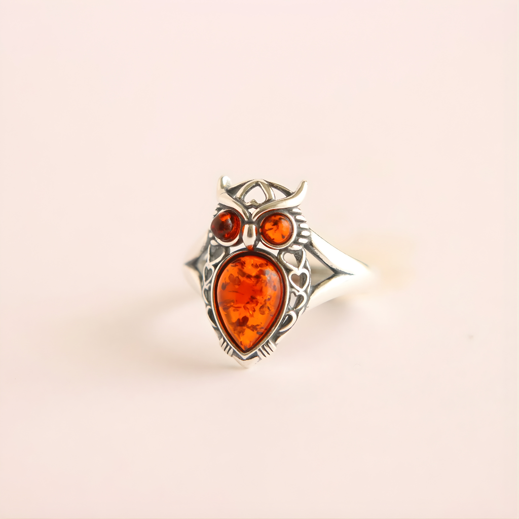 Silver owl amber ring with amber heart and gemstones on a beige background