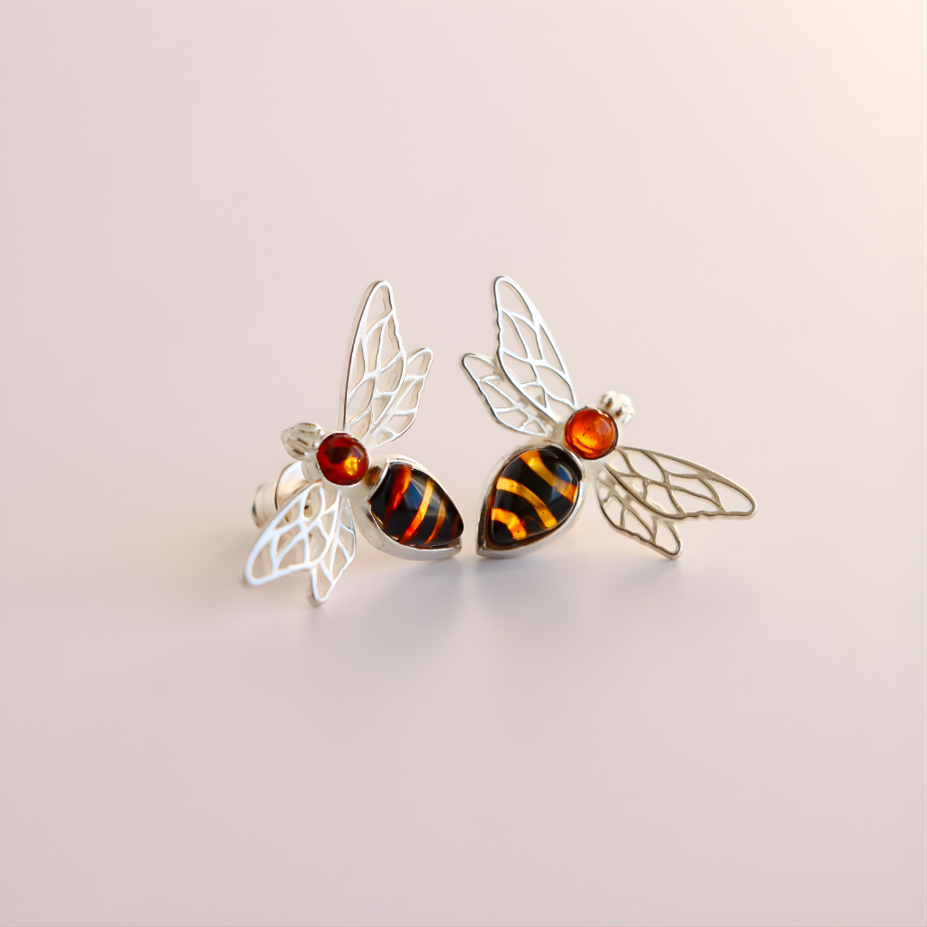 Silver bee-shaped amber earrings with amber accents on a light pink background
