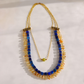 A gold-tone multi-strand statement necklace featuring blue and amber-orange stone beads, displayed on a light off-white background.