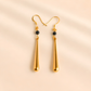 Gold drop earrings with black beads on a beige background