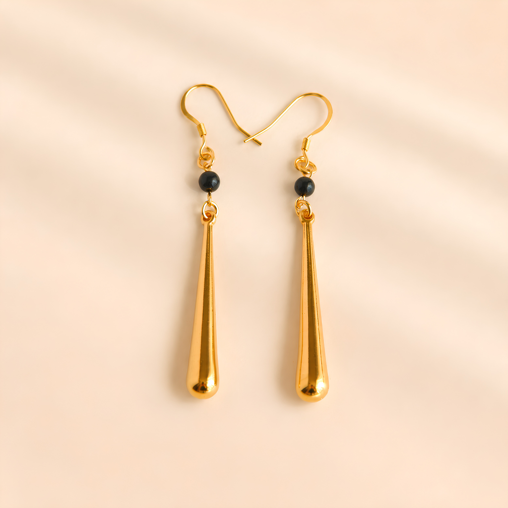Gold drop earrings with black beads on a beige background