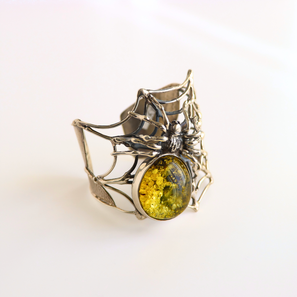 A silver spider amber bracelet with a large oval yellow-green glittery stone, photographed on a clean white background.