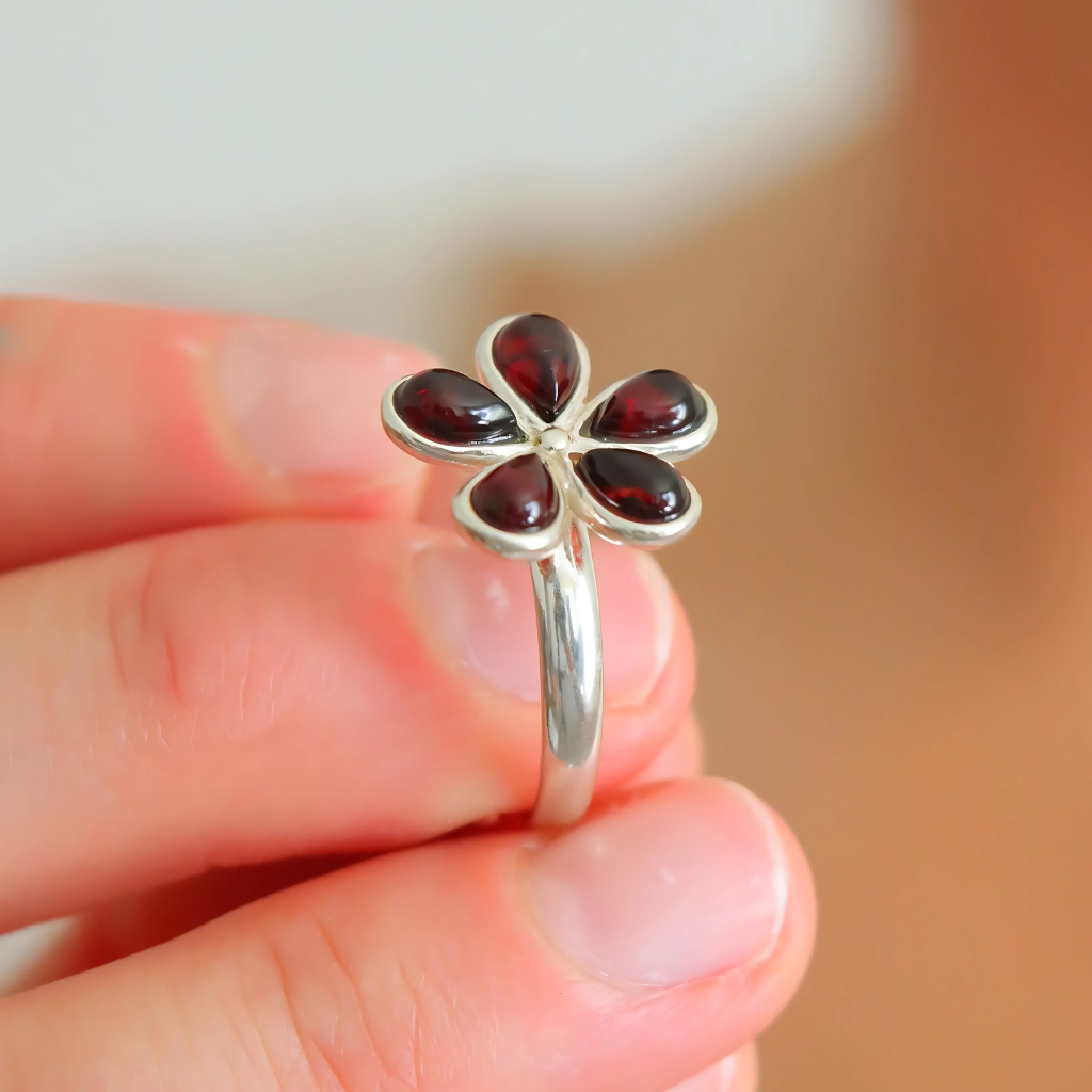 Silver ring with red gemstones held on a blurred background