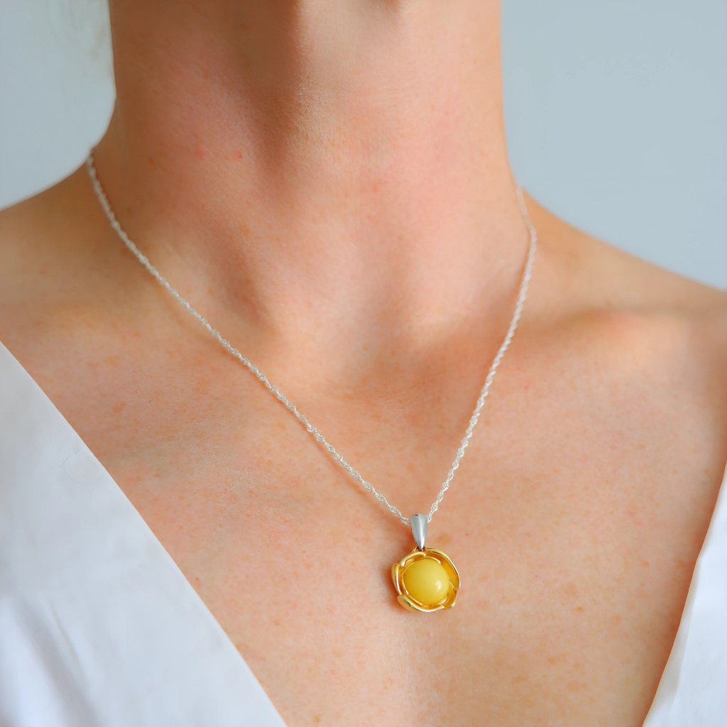 Yellow pendant necklace on a person wearing a white top against a light background
