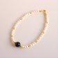 Pearl necklace with a black bead on a light pink background