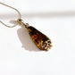 A teardrop-shaped green amber pendant necklace with a silver-toned filigree accent on one end, hanging from a silver chain against a bright white background.