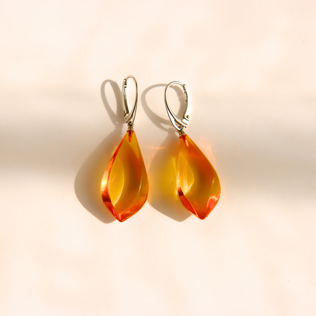 A pair of teardrop-shaped Baltic amber drop earrings with silver leverback hooks, displayed on a warm beige background with soft shadows.