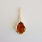 Gold amber necklace  with a brown gemstone on a light gray background