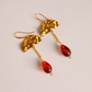 A pair of gold drop vintage Lucite Bead earrings with textured tops, short chain links, and teardrop-shaped red Lucite beads, shown on a light beige background.
