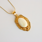 Gold amber necklace pendant with a white stone on a light gray background