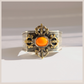 A wide silver-toned amber cuff bracelet with ornate gold-toned filigree details and a central oval orange stone, photographed on a light neutral background.