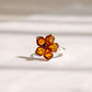 A silver amber flower ring featuring a five-petal flower design made from cognac Baltic amber with a small dark red center stone, set against a softly lit white background.