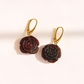 A pair of amber rose-shaped drop earrings with dark reddish-brown carved petals and gold leverback hooks, displayed on a clean white background.