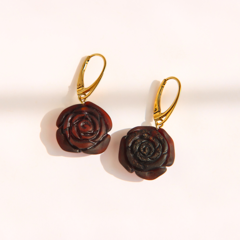 A pair of amber rose-shaped drop earrings with dark reddish-brown carved petals and gold leverback hooks, displayed on a clean white background.