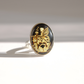 A silver amber cameo ring with an oval black amber cabochon featuring a carved fairy and floral design, photographed on a white surface with a soft shadow.
