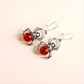 Spider-shaped sterling silver earrings with orange centers on a light background