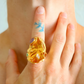 Close-up of a hand wearing a gold cocktail ring with a purple gemstone.