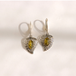 A pair of silver filigree dangle amber earrings with marquise-cut green gemstones, displayed on a light cream background with soft shadows.