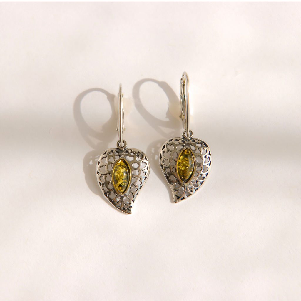 A pair of silver filigree dangle amber earrings with marquise-cut green gemstones, displayed on a light cream background with soft shadows.